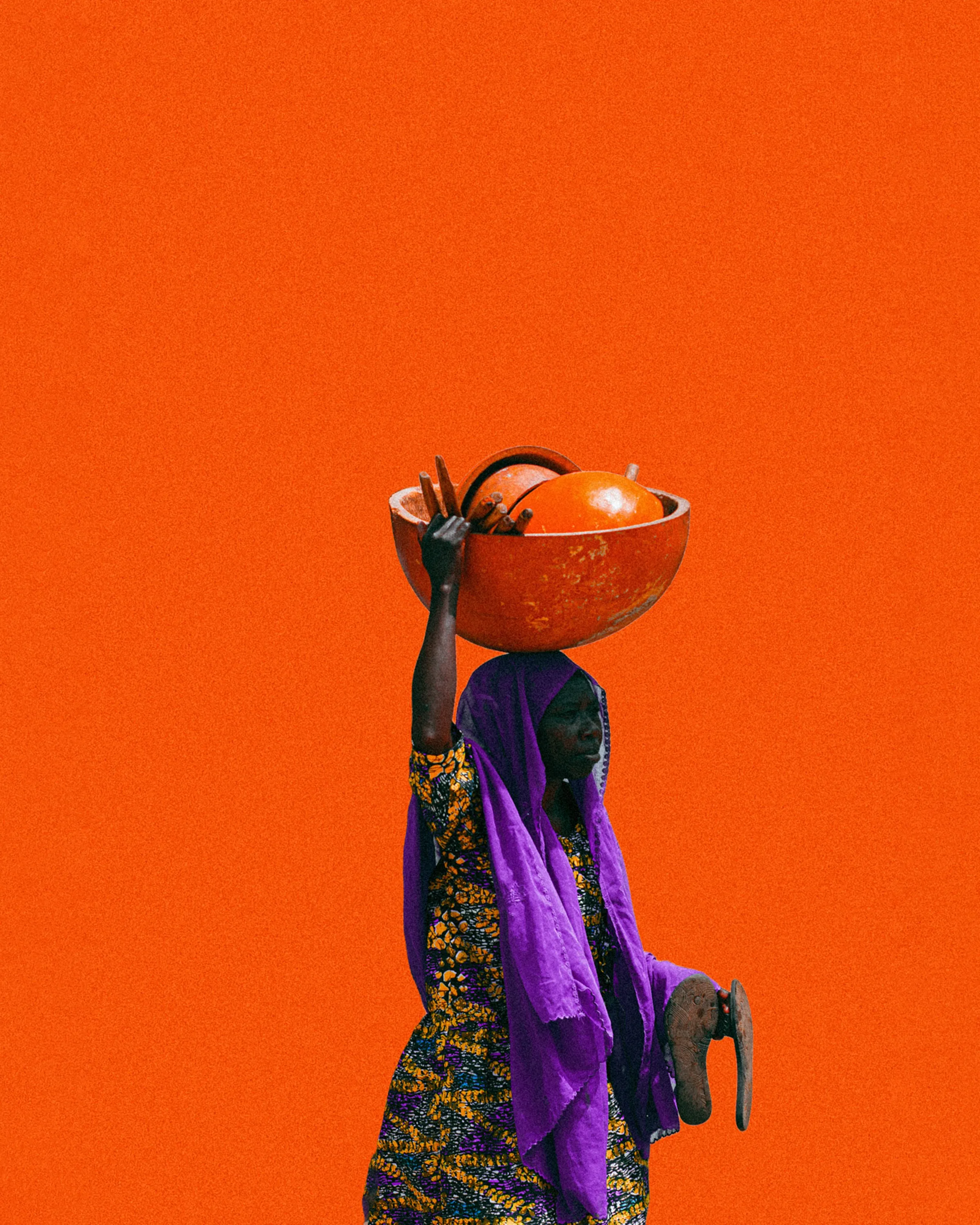 A woman carrying a calabash bowl on her head against an orange wall